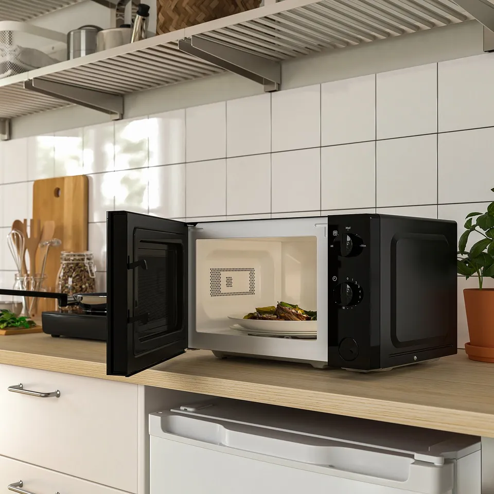 Black and white microwave oven open displaying food inside, placed on a wooden countertop next to kitchen plants.