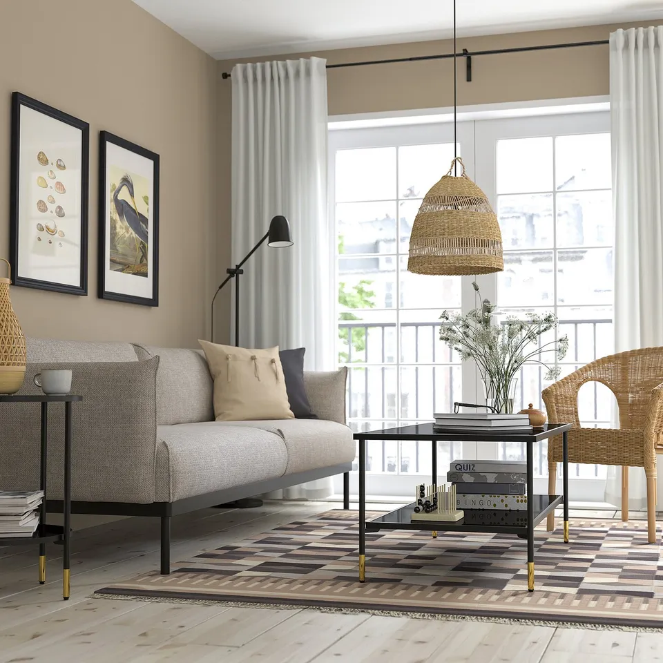 Modern living room with black ÄSPERÖD coffee table & gold accents. Minimalist design under pendant light, with sofa & wicker chair.