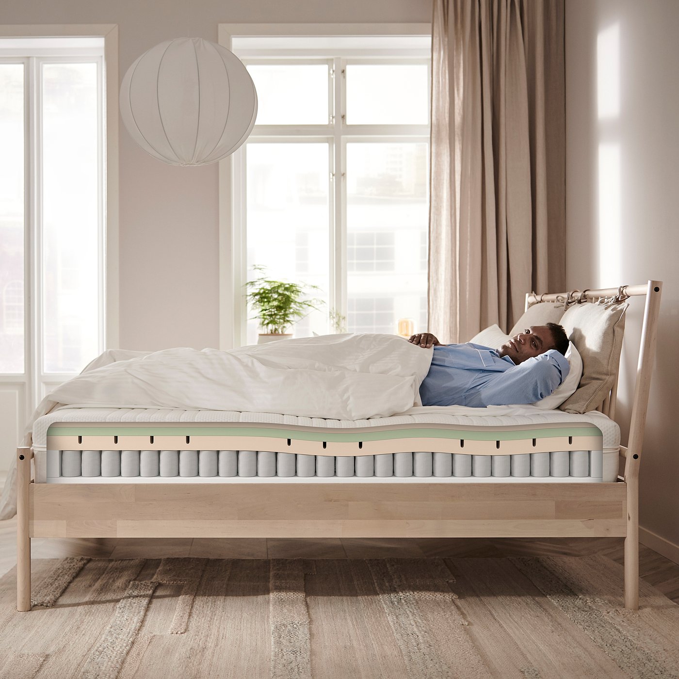 Person resting on a firm, white ÅNNELAND hybrid mattress with foam and spring layers.