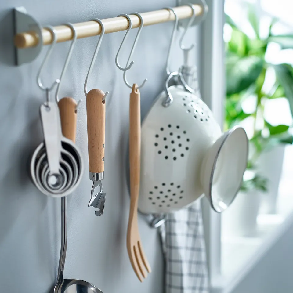 Kitchen tools hang neatly on wall hooks. Includes measuring cups, can opener, strainer, and spatula, all with wooden handles, ready for use.