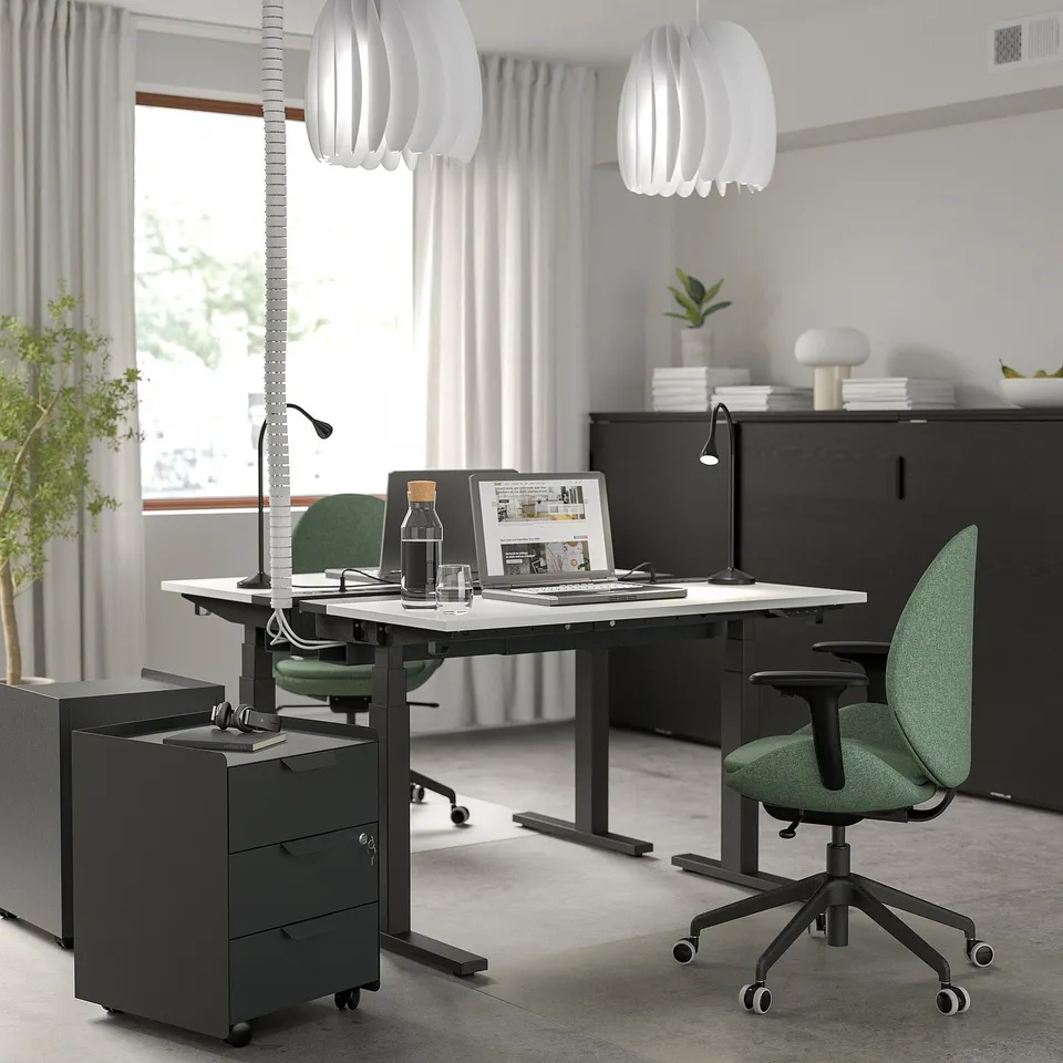 Modern office setup with MITTZON black sit/stand desk, green chairs, sleek pendant lamps. Clean, minimalist design with ample workspace.