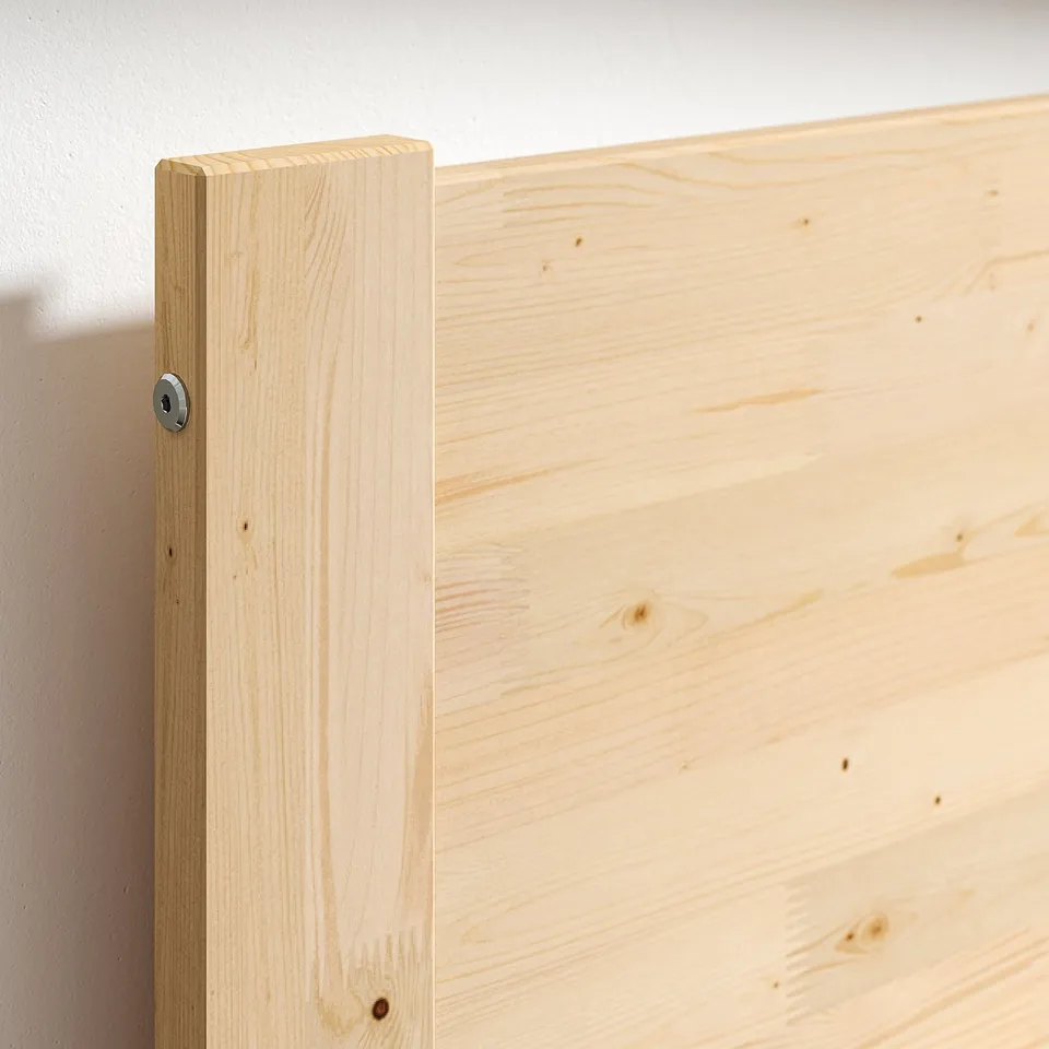 Close-up of a wooden bed frames corner, showcasing natural pine texture and a metal bolt.