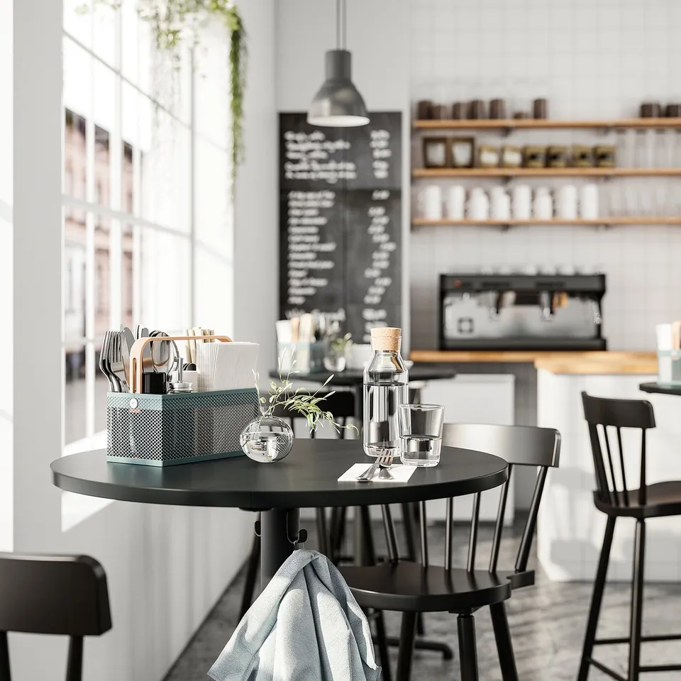 Modern café with black tables and chairs. VIMPELFISK cutlery organiser on table, chalkboard menu behind.