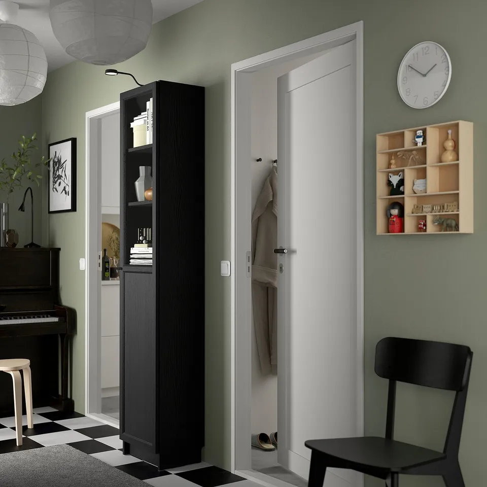 Modern room with BILLY bookcase, black chair, and white door. Bookcase offers ample storage, stylish decor includes clock, shelf, piano, and lighting.