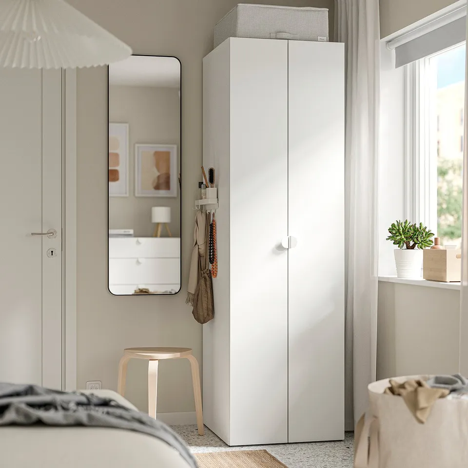 Modern bedroom with white STUK cabinet next to a window, smaller than nearby wardrobe.