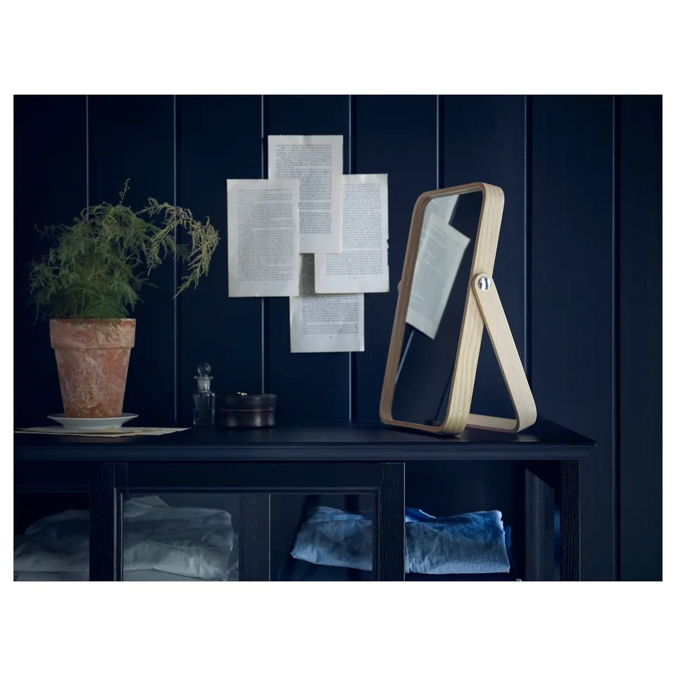 Dark navy shelf with light wood triangle mirror, plant, papers, and folded blue towels.