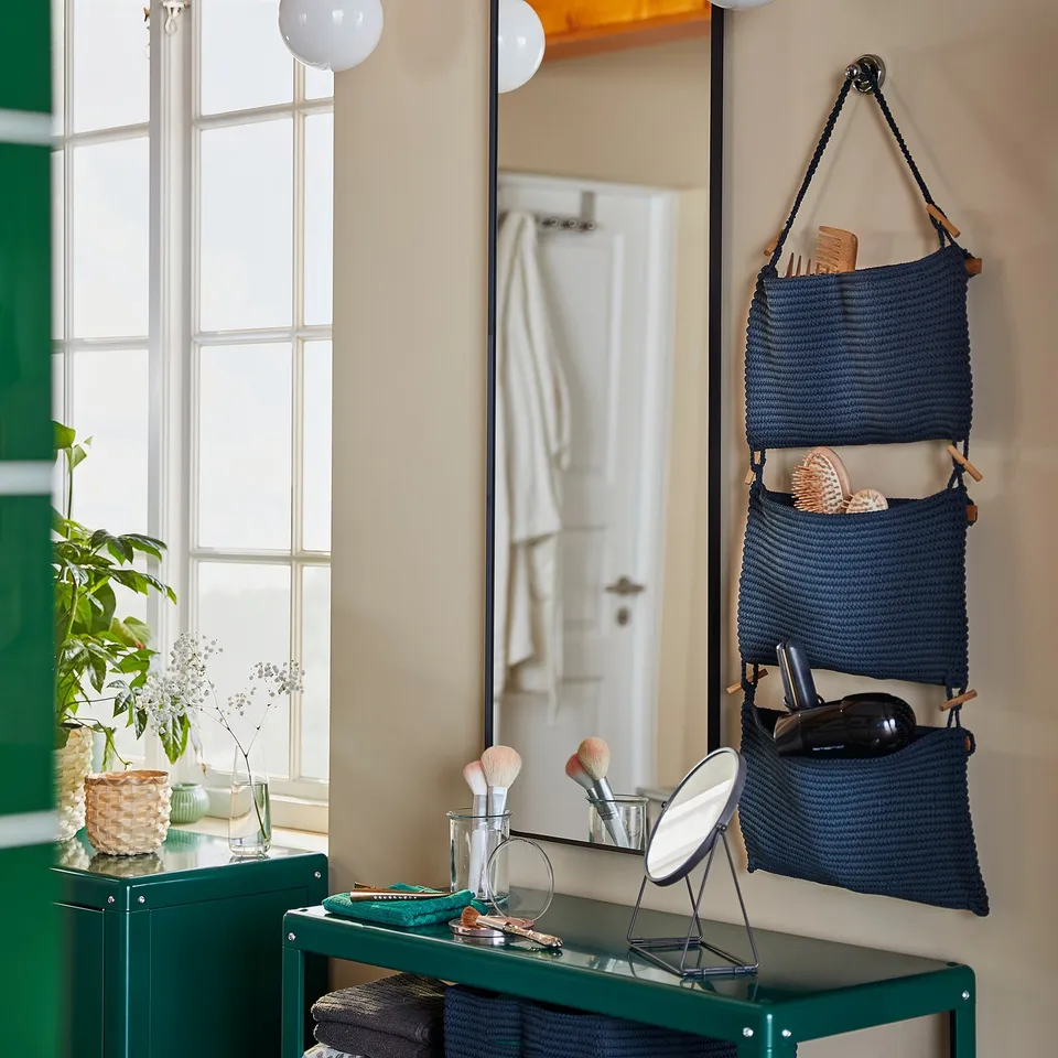 Bathroom with green cabinet, round mirror, blue wall baskets, plants, and makeup items.
