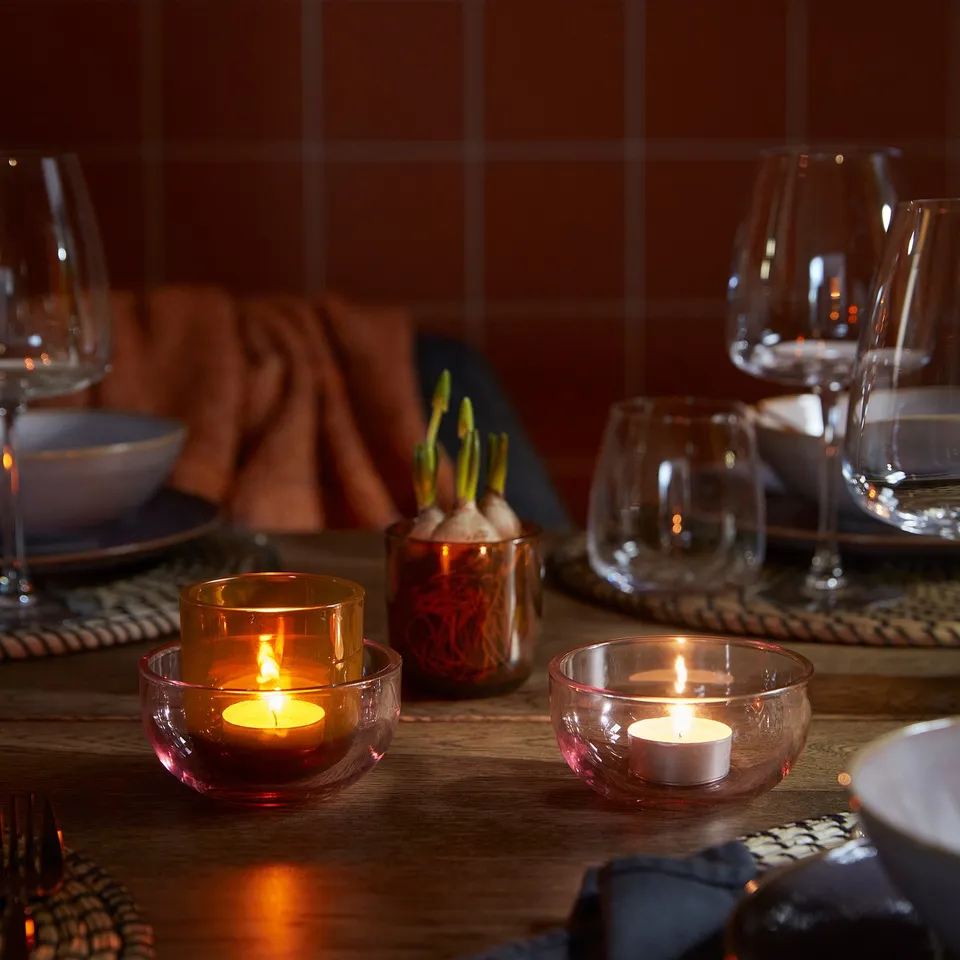 Wooden table set with lit candles, glasses, and plates, creating a warm ambiance.