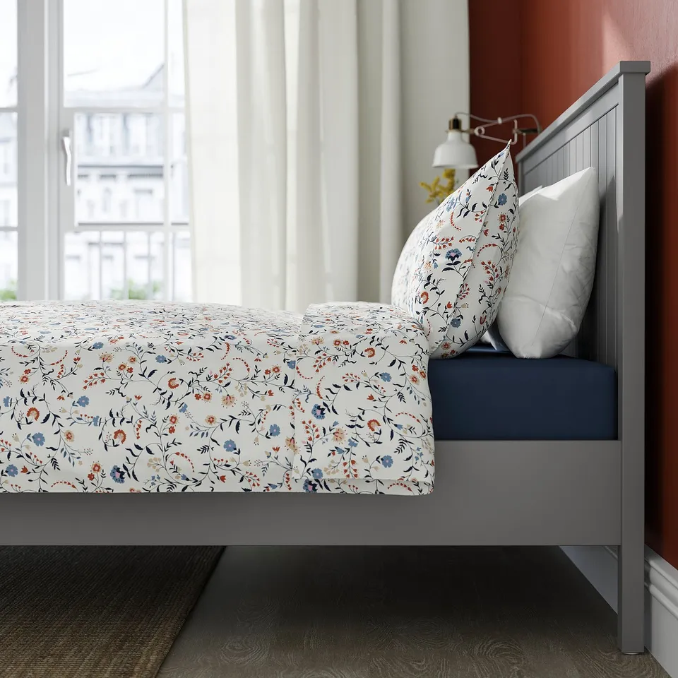 A grey GULLABERG bed with a floral bedspread and white pillows. The bed has a centre support beam.