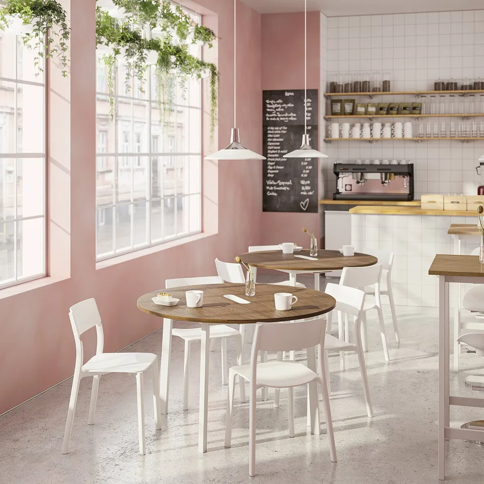 Modern minimalist café with round MITTZON tables, white chairs, pink walls, large windows, hanging plants, and chalkboard menu.
