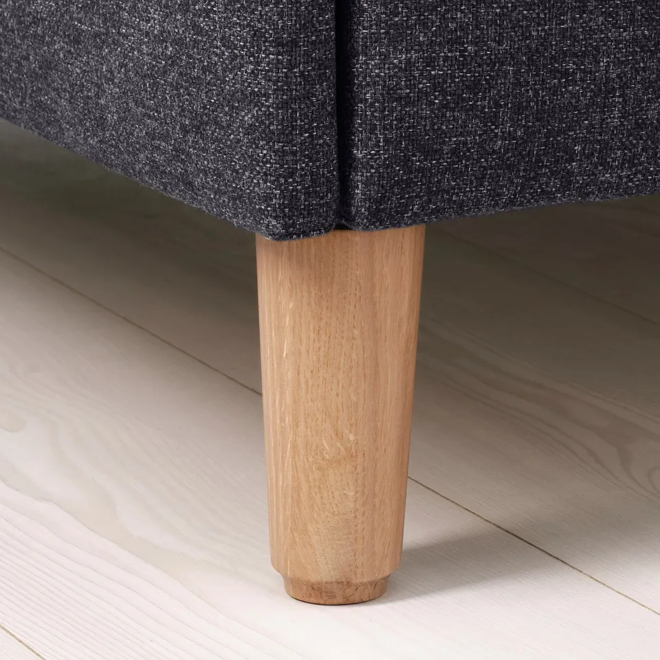 Close-up of modern bed base with sleek, wooden legs in light brown and sturdy, textured dark grey upholstery. Floor visible.