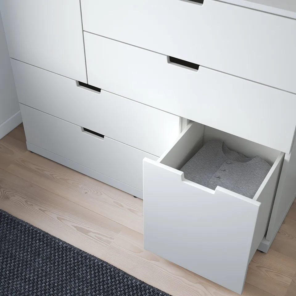 White chest of drawers, one drawer open revealing grey fabric interior with folded items inside, on a wooden floor with a grey rug.