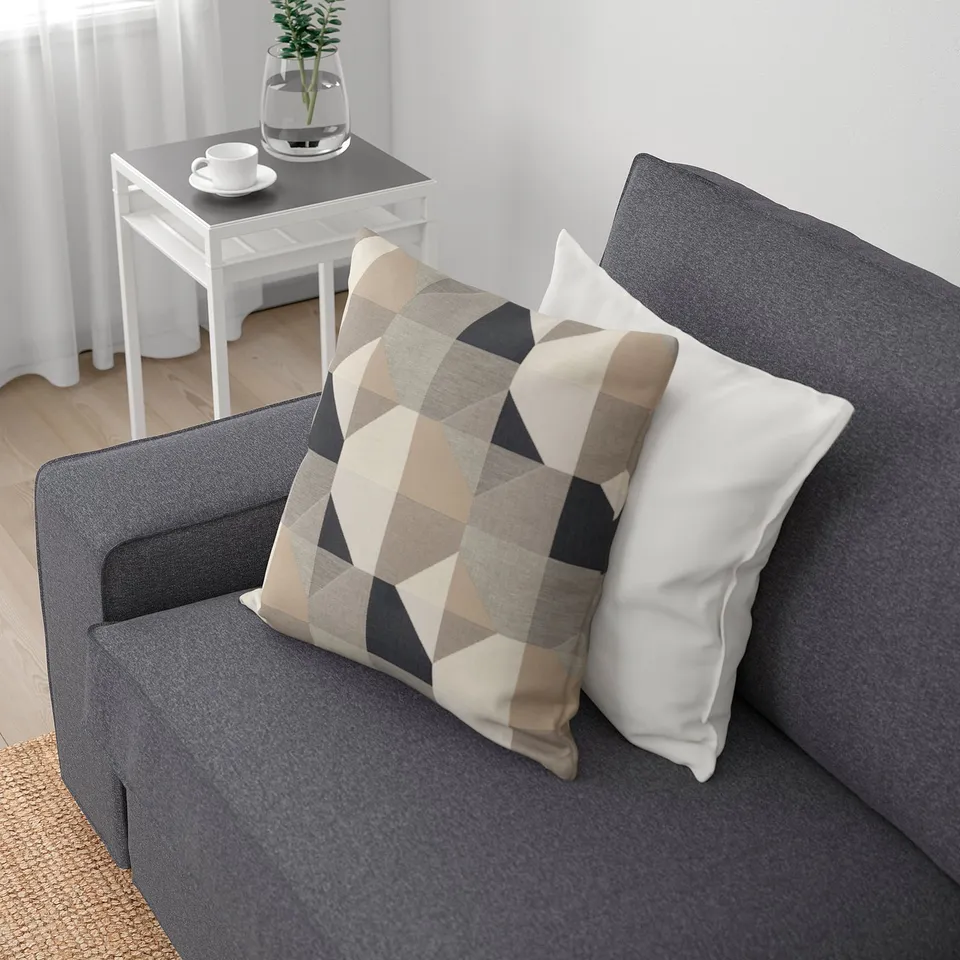 Grey KIVIK sofa with plaid and white pillows, wooden side table with coffee set and plant.