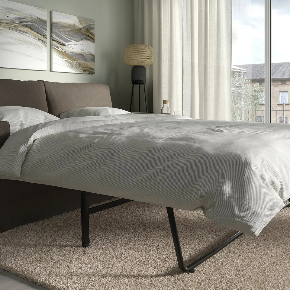 Modern sofa-bed, grey with black legs, near window, converts to bed.