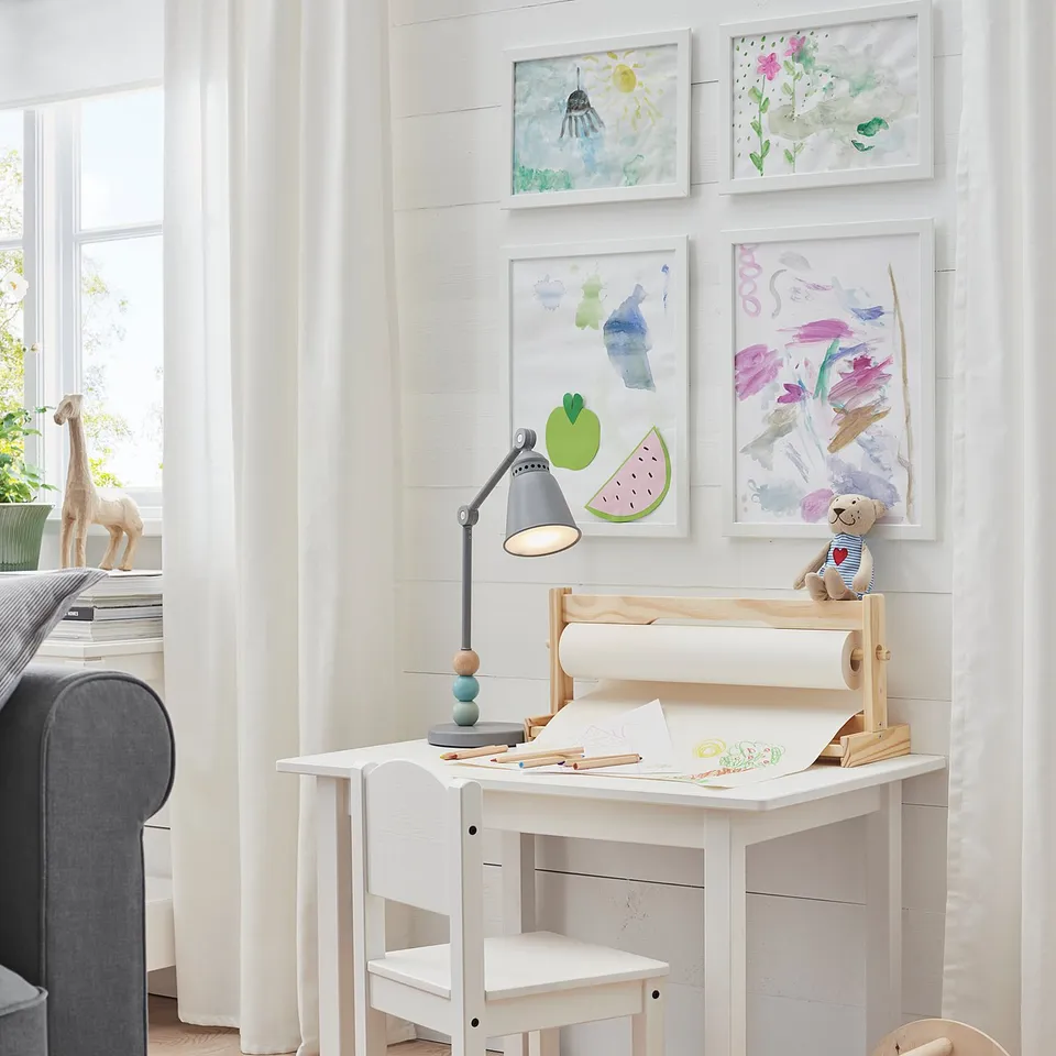 Kids desk with chair, lamp, artwork, by window with couch, toys.