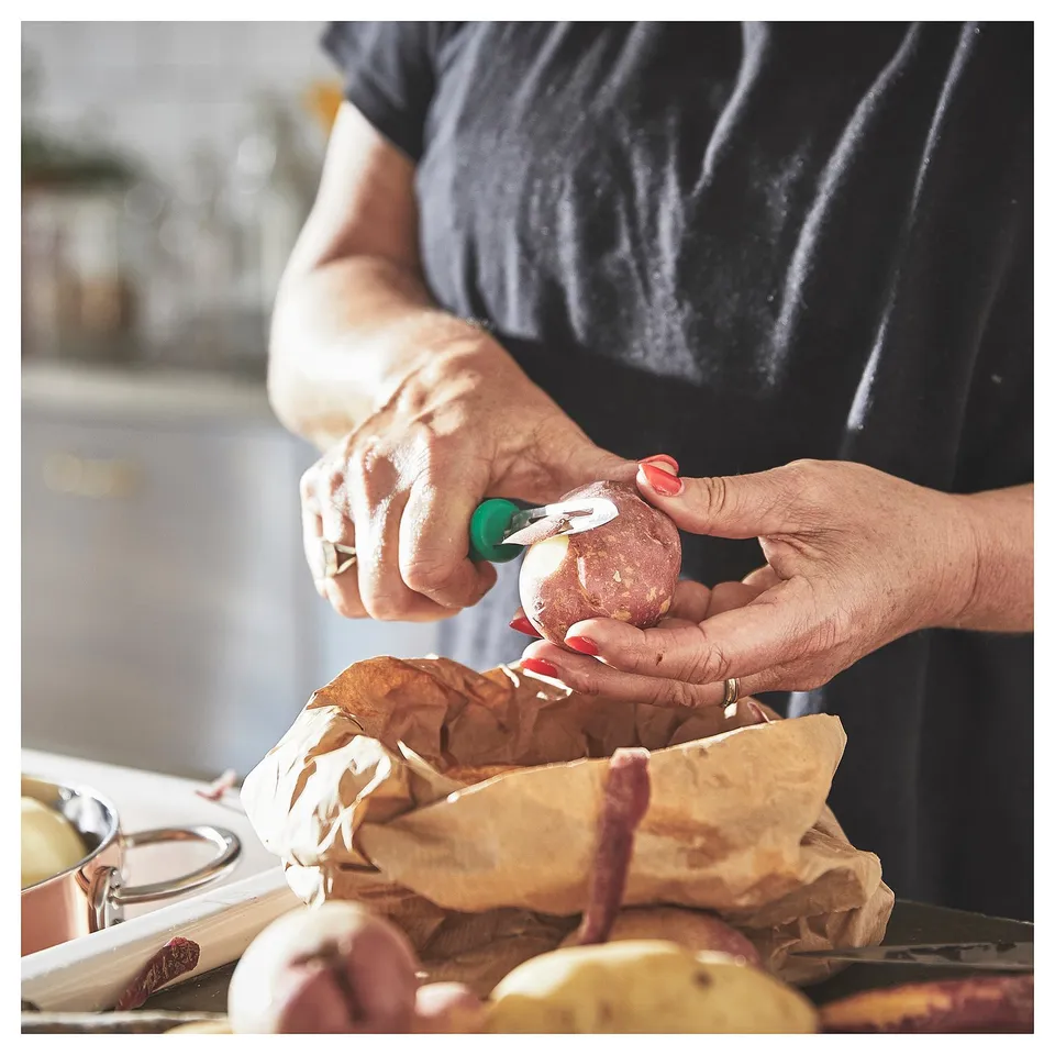 Peeling potatoes with green-handled tool.