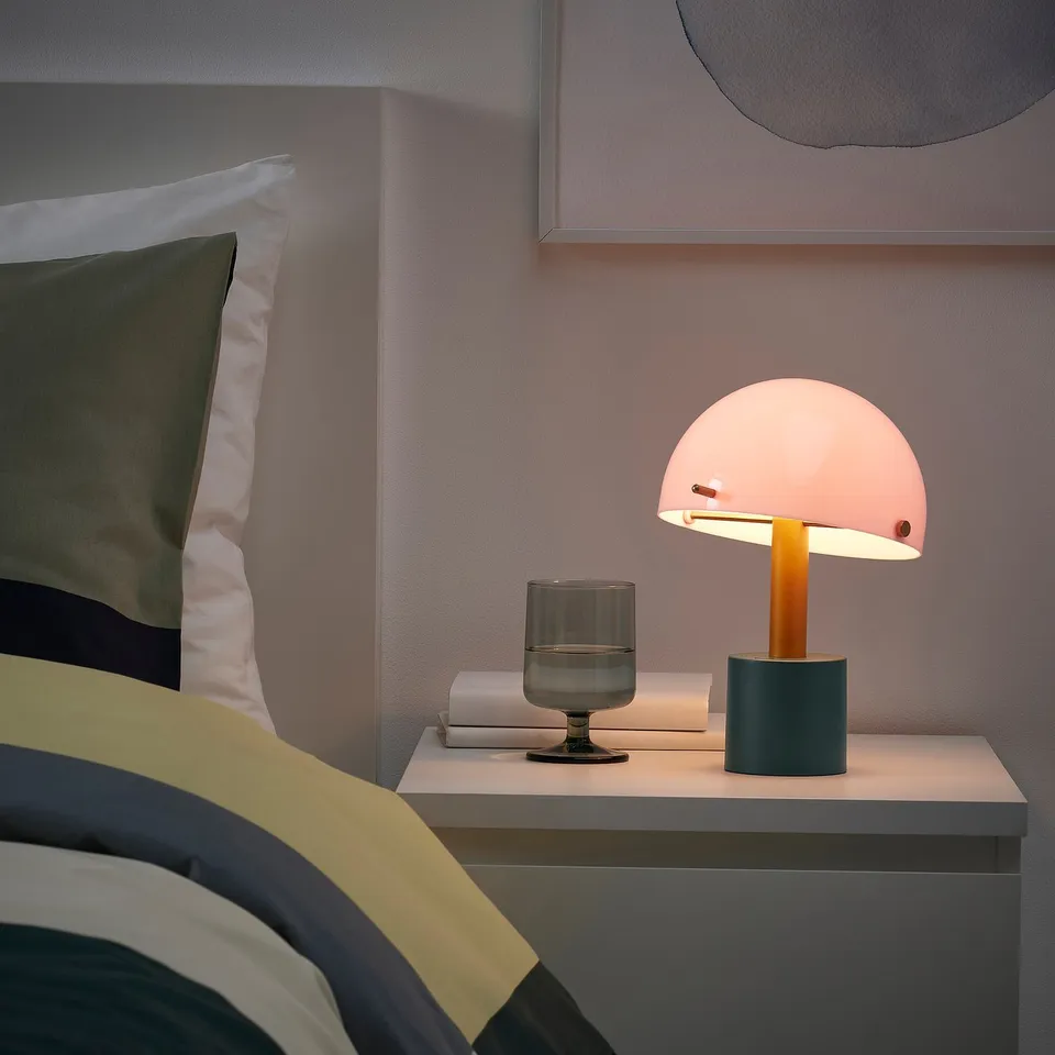 Cosy bedroom with colourful blanket, stylish bedside table, NÖDMAST lamp, and small books.