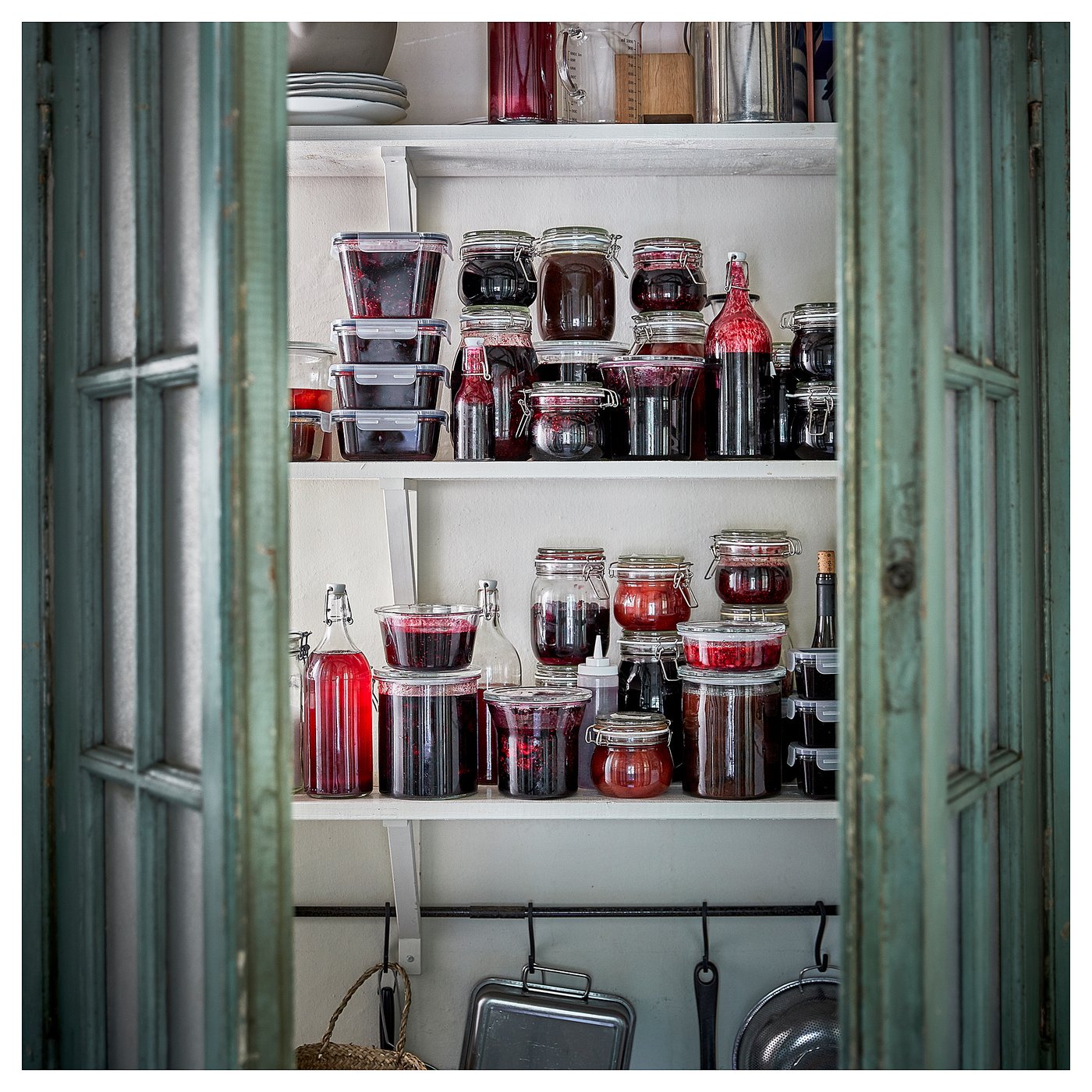 Shelves with glass jars filled with red jelly. Wooden cabinet doors frame the shelves. Jars vary in size and shape, some with lids, others open.