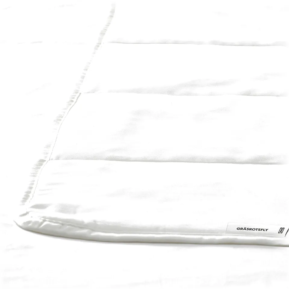 White duvet with elegant, smooth texture and subtle stitching detail. Brand label visible on one corner, indicating high-quality fabric and design.