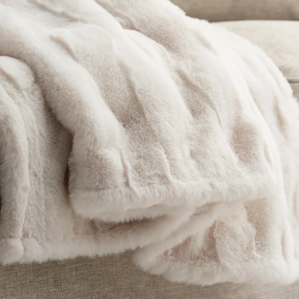 Soft, fluffy white blanket draped on a bed. Intricate wavy texture, inviting touch, appears luxurious and cosy.