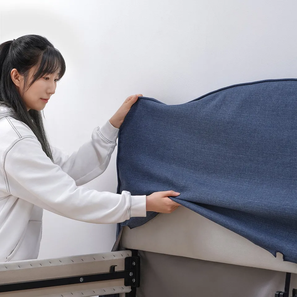 A person is putting on a grey cover on a bed frame as part of updating the beds look.