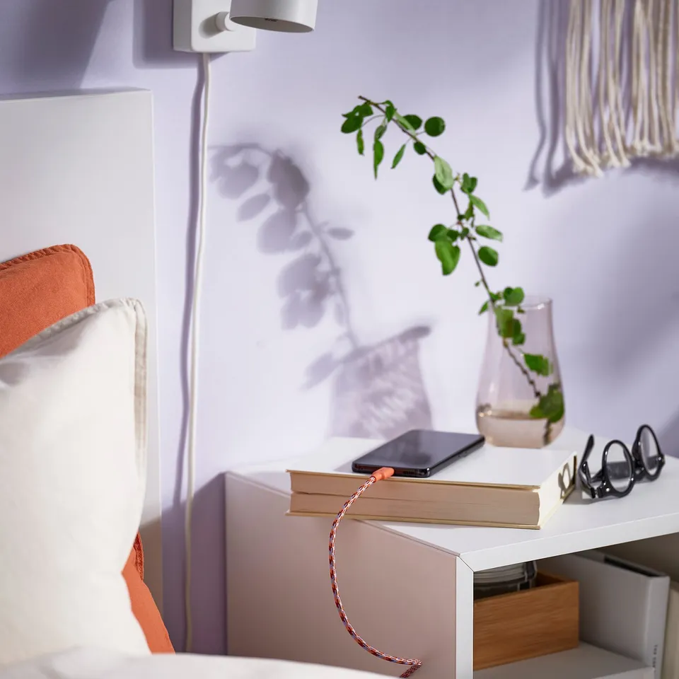 Bedside setup with LILLHULT usb-c cable, charging phone on books, near plant and lamp.