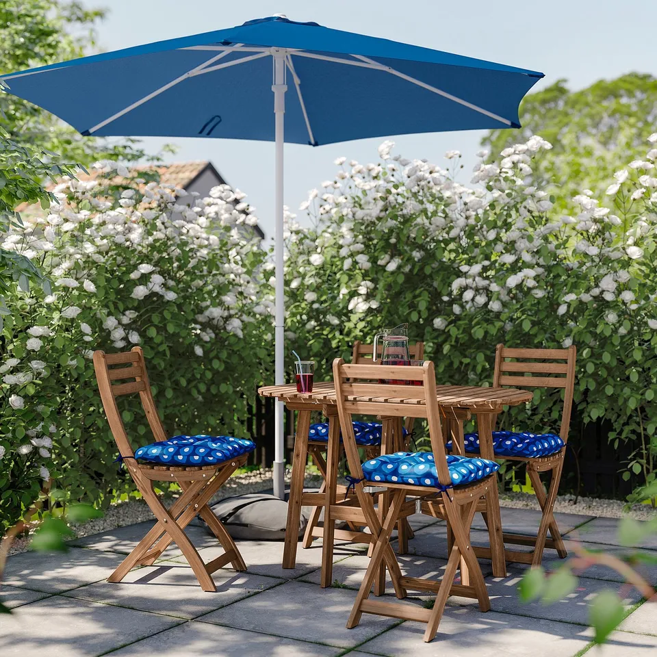 Blue patio set with wooden table, polka dot chairs, and umbrella, surrounded by white flowers.