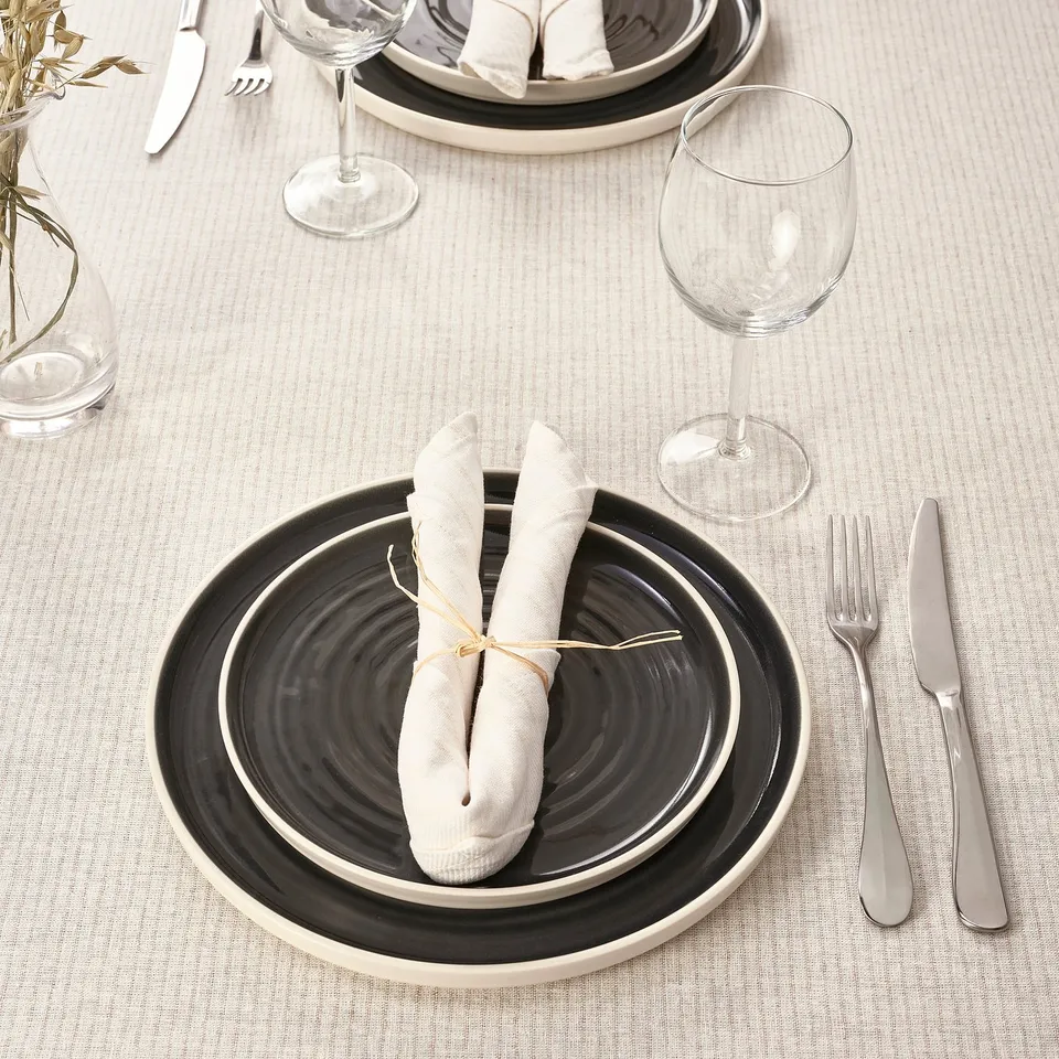 Table set with black and white plates, rolled napkins, silverware, and wine glasses on a beige tablecloth.