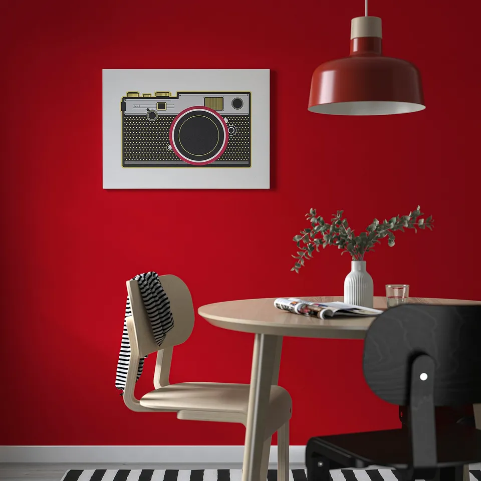 Modern dining setup with red wall, vintage camera canvas, pendant lamp, striped & black chairs, newspaper, vase greenery, PJÄTTERYD print.