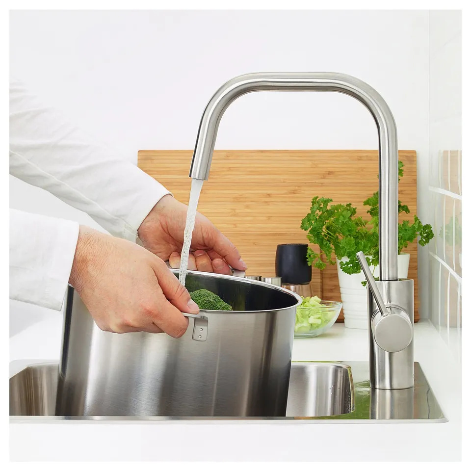 Person washes vegetables under ÄLMAREN tap, saving water and energy.