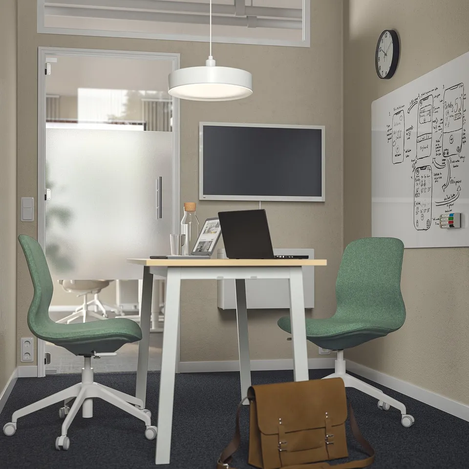 Modern office with MITTZON white table & green chairs, flat screen, laptop & bag.