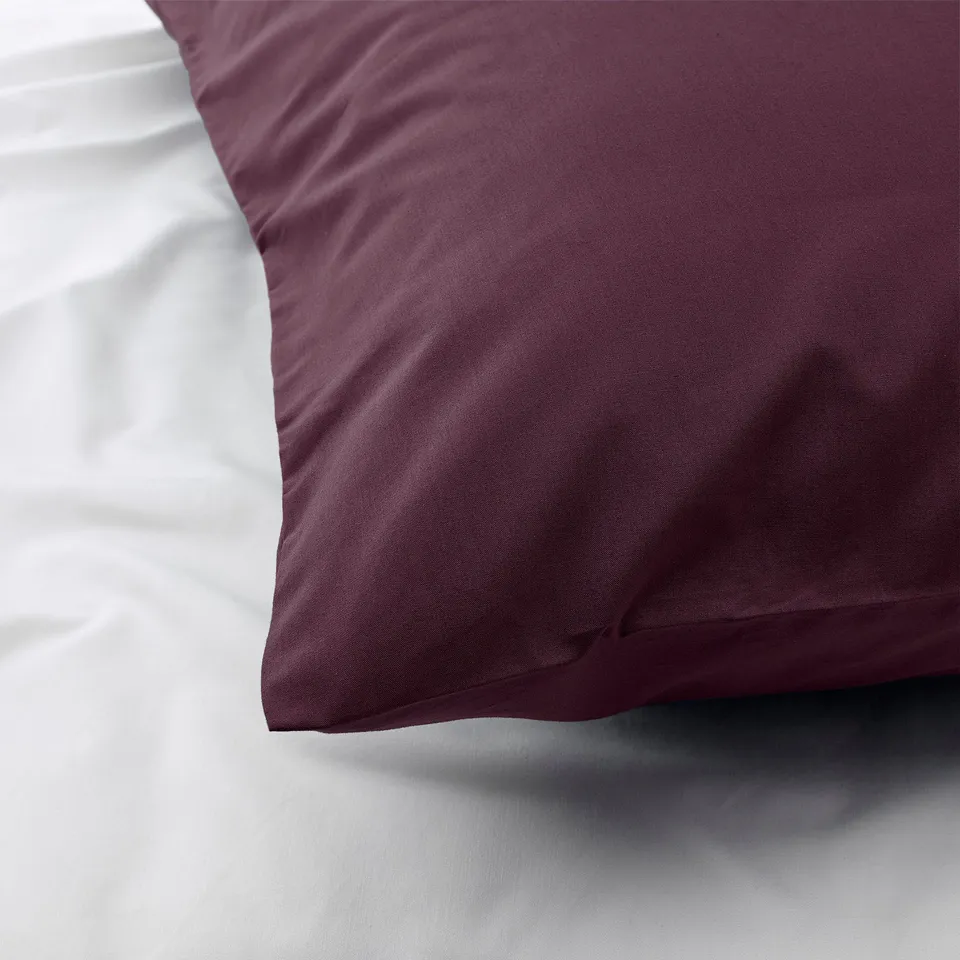 Close-up of burgundy pillowcase with crisp, soft texture on white bedding, showcasing high-quality cotton and lyocell blend.