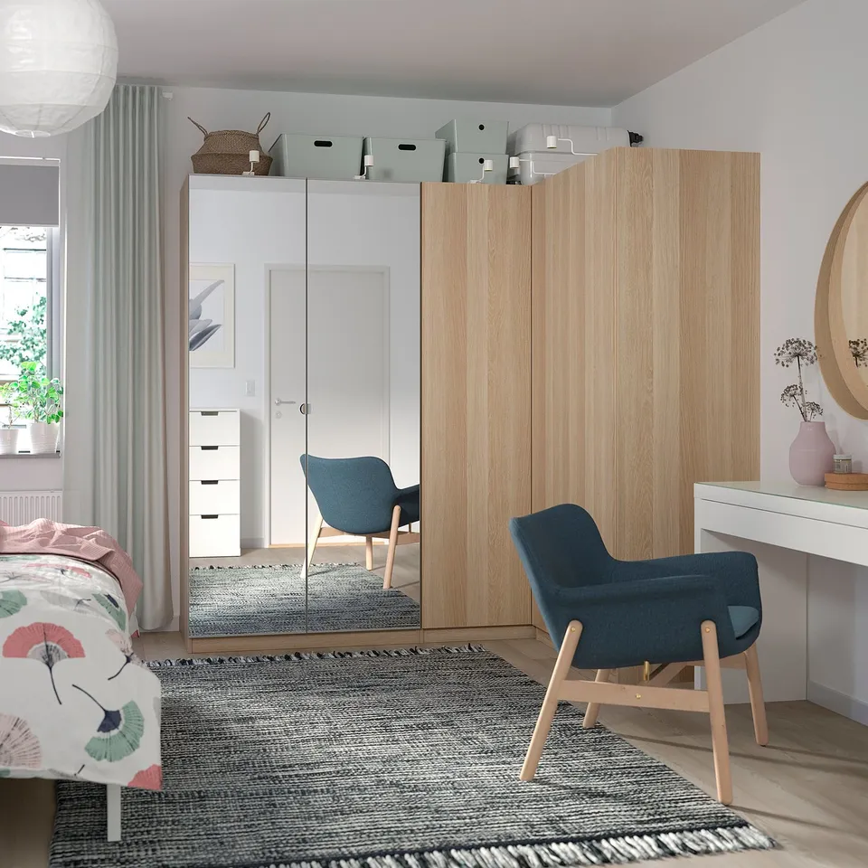 Bedroom with wooden FORSAND wardrobe, blue chair, rug, and white desk.