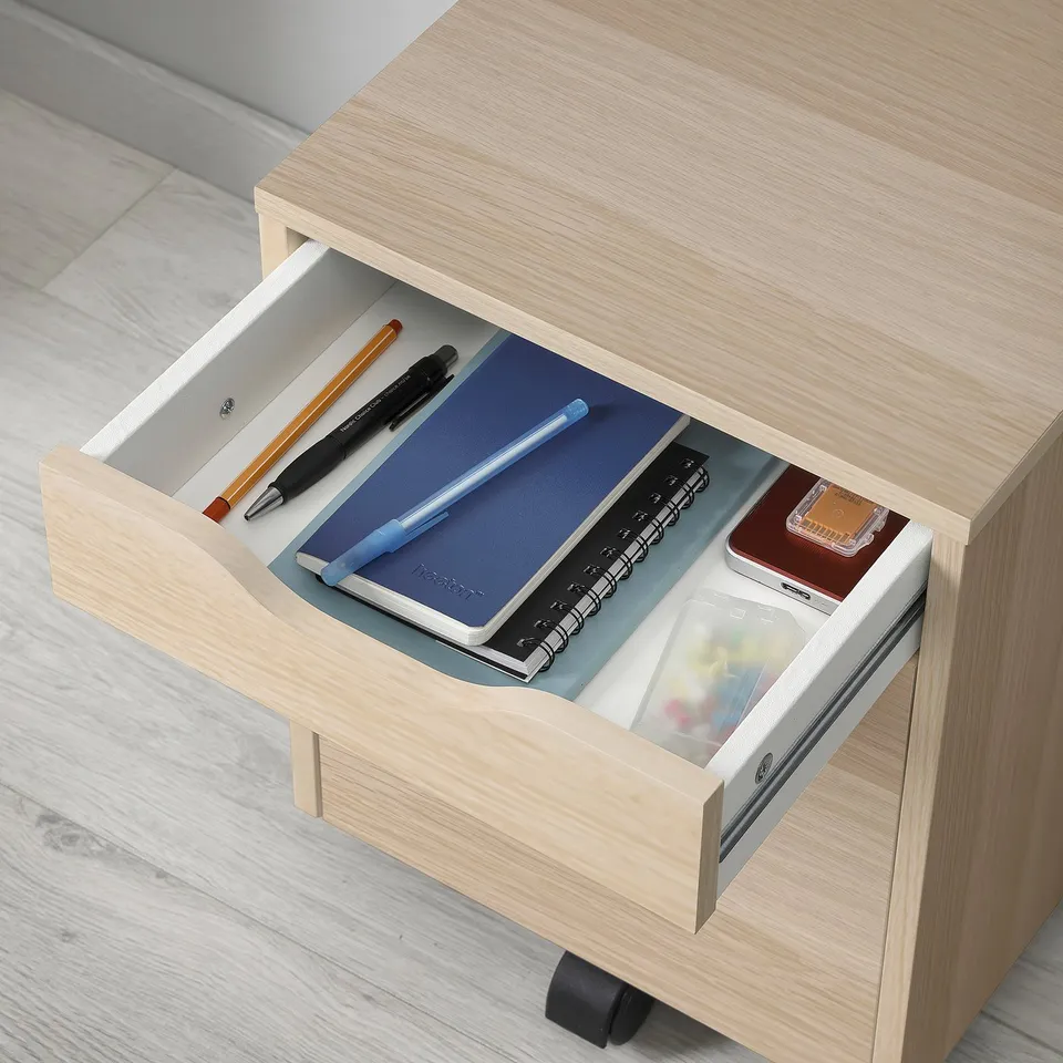 Open wooden desk drawer showing pens, notebooks, and office supplies organised.