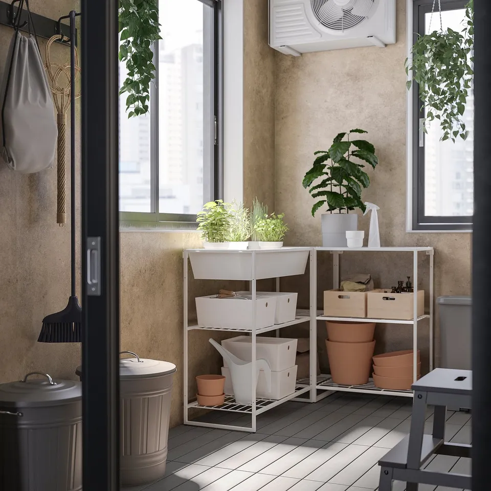 Modern indoor/outdoor storage area with white JOSTEIN shelves, potted plants, tools, and bins.