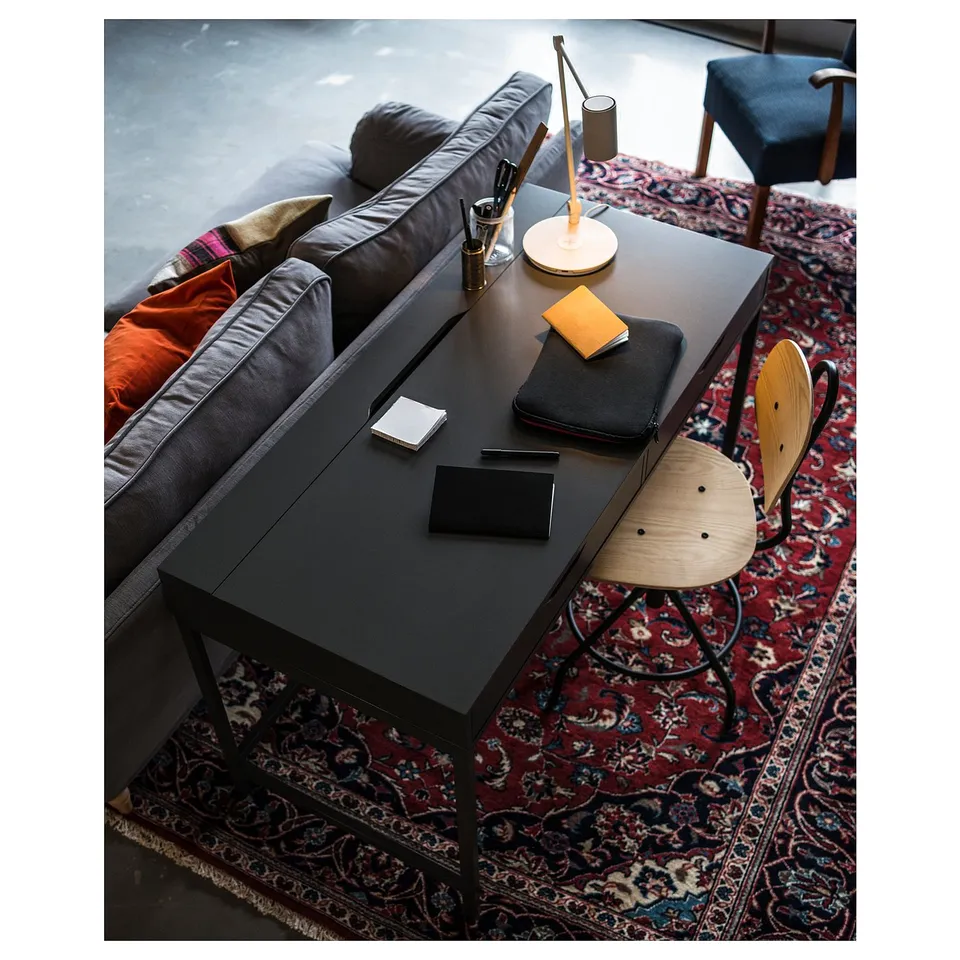 Cosy room with grey sofa, black desk, wooden chair, colourful rug, and lamp.