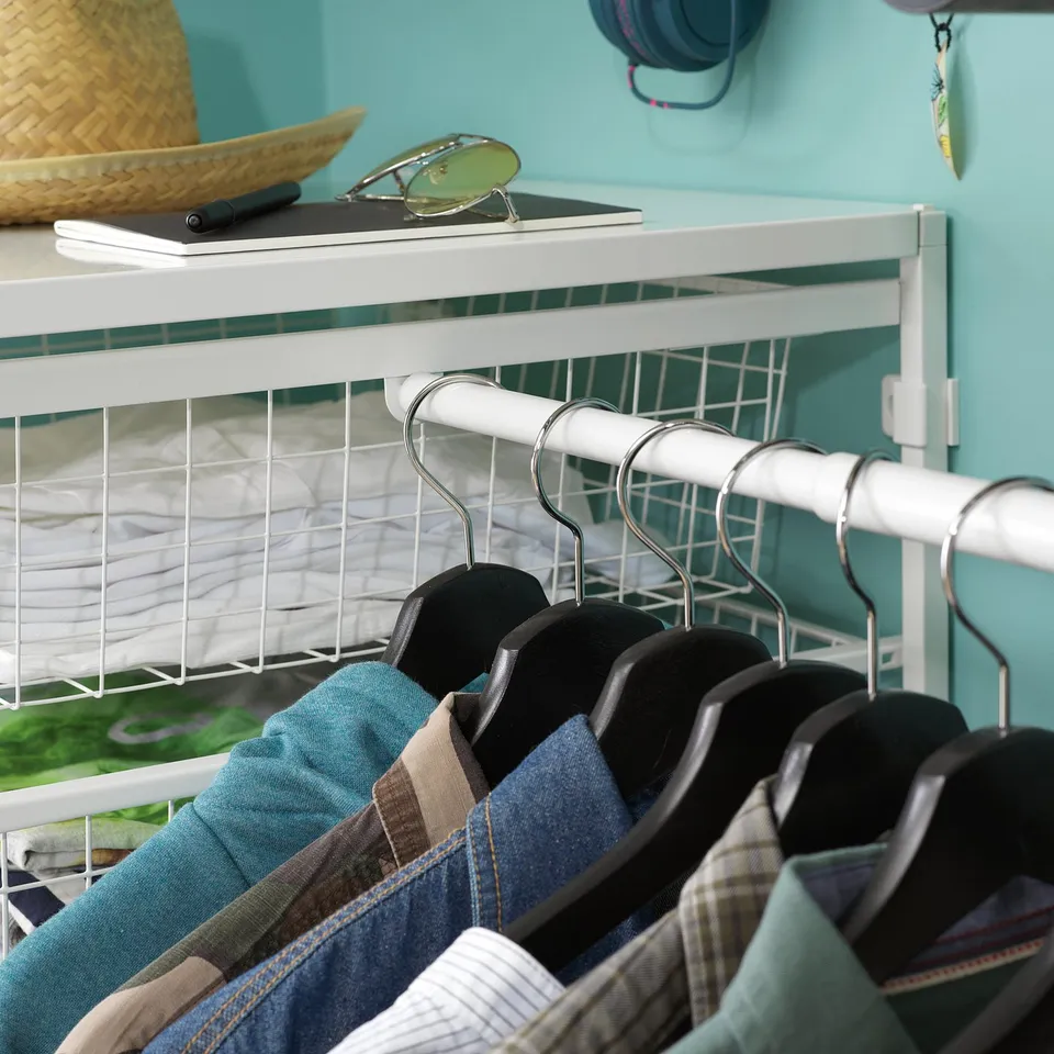 White JONAXEL wardrobe with hangers and folded clothes, blue wall background.