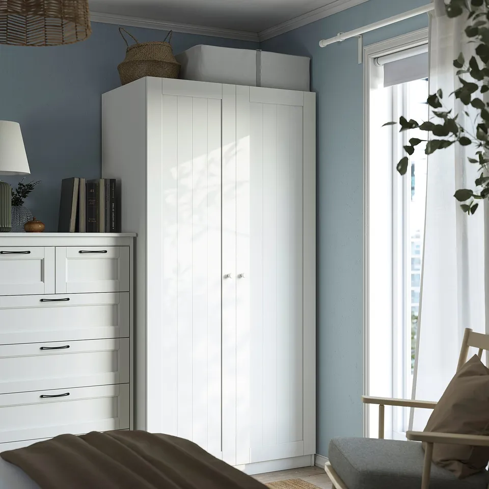 Minimalist bedroom with tall white PAX wardrobe and dresser, surrounded by light blue paint. Wardrobe is larger than other items.