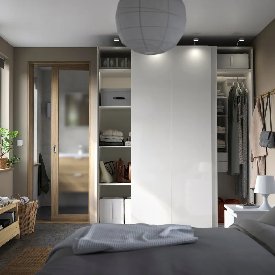 Bedroom with white PAX wardrobe, sliding doors, lighting, clothes, grey bed, wooden door, round lamp.