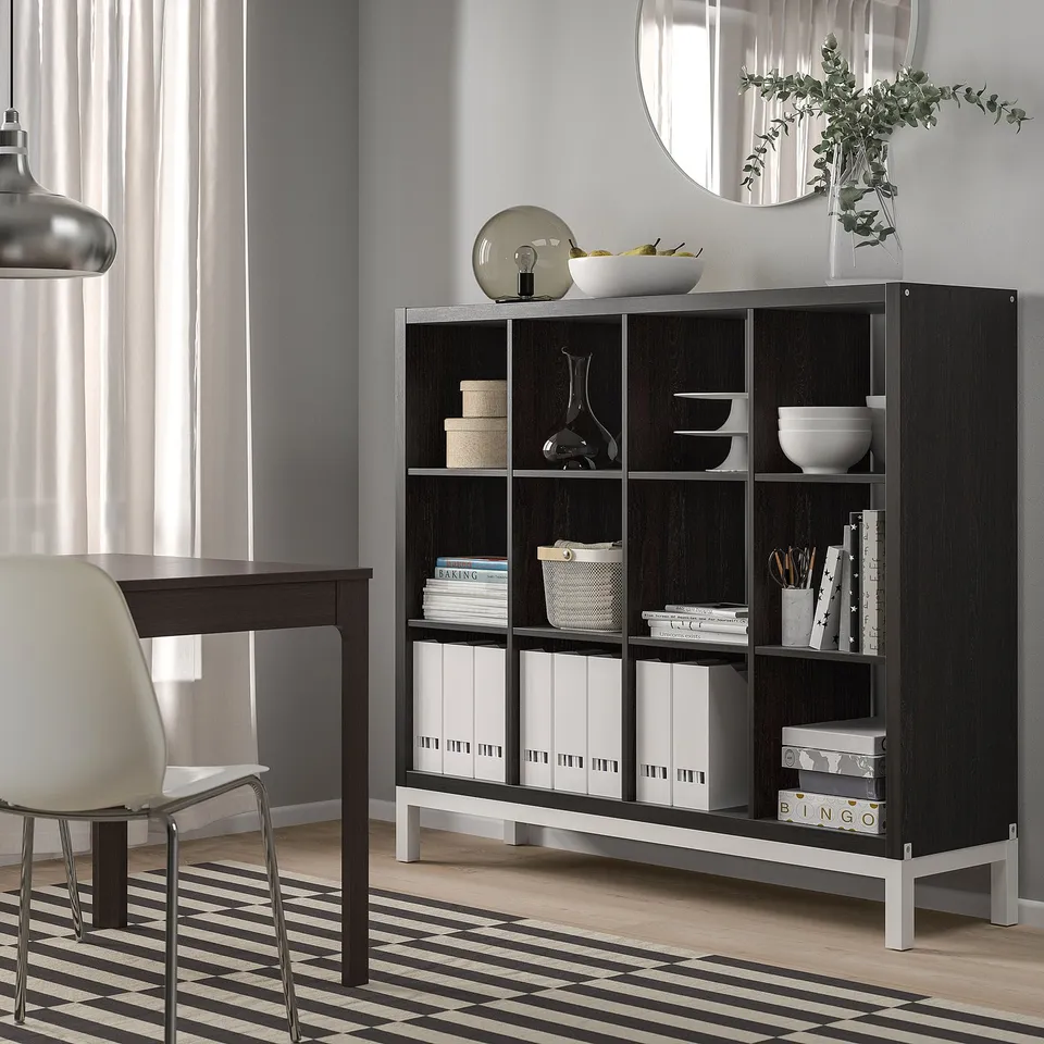 Black KALLAX shelving, modern, 4x4, holds books, bowls, and decor, fits well near white desk and chair.