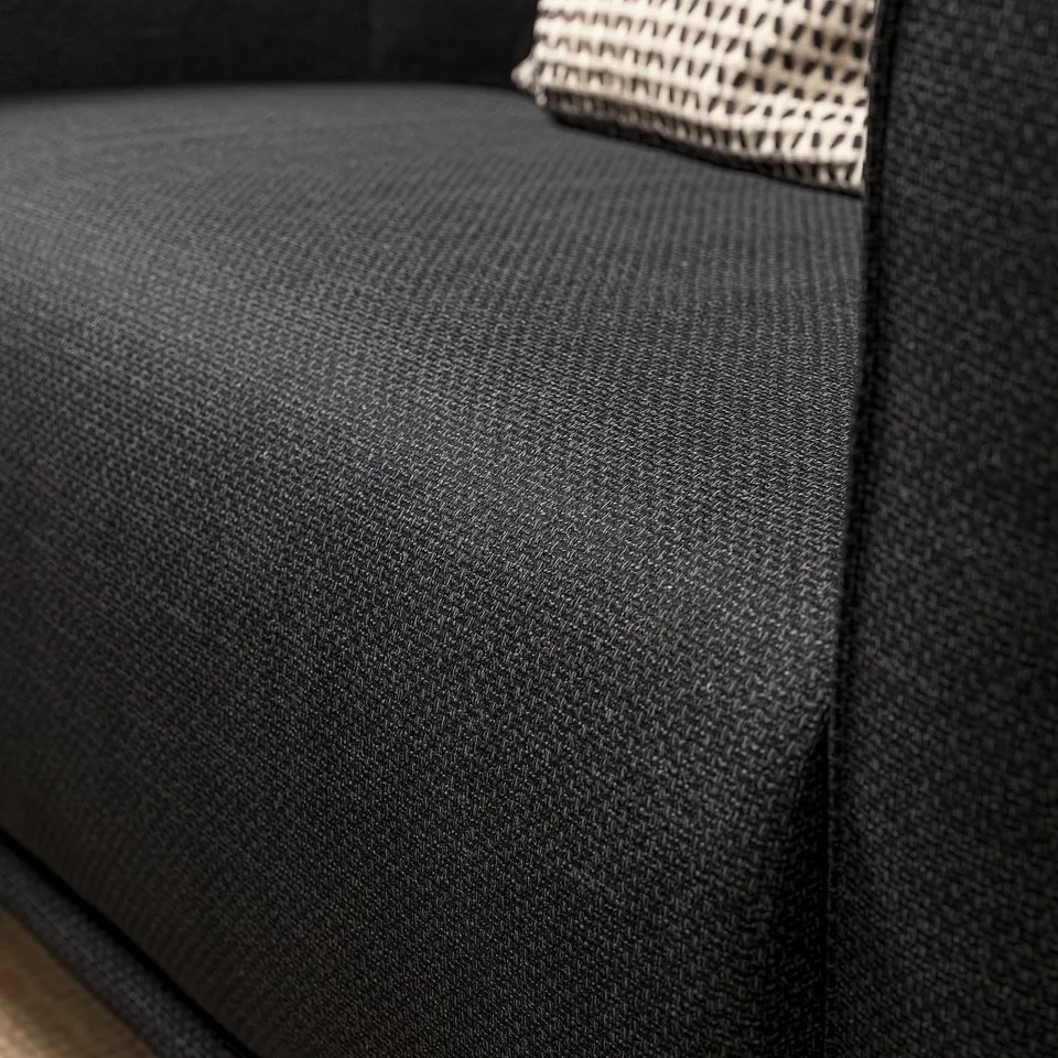 Dark grey textured fabric armchair close-up. Soft, rounded design with deep seat.