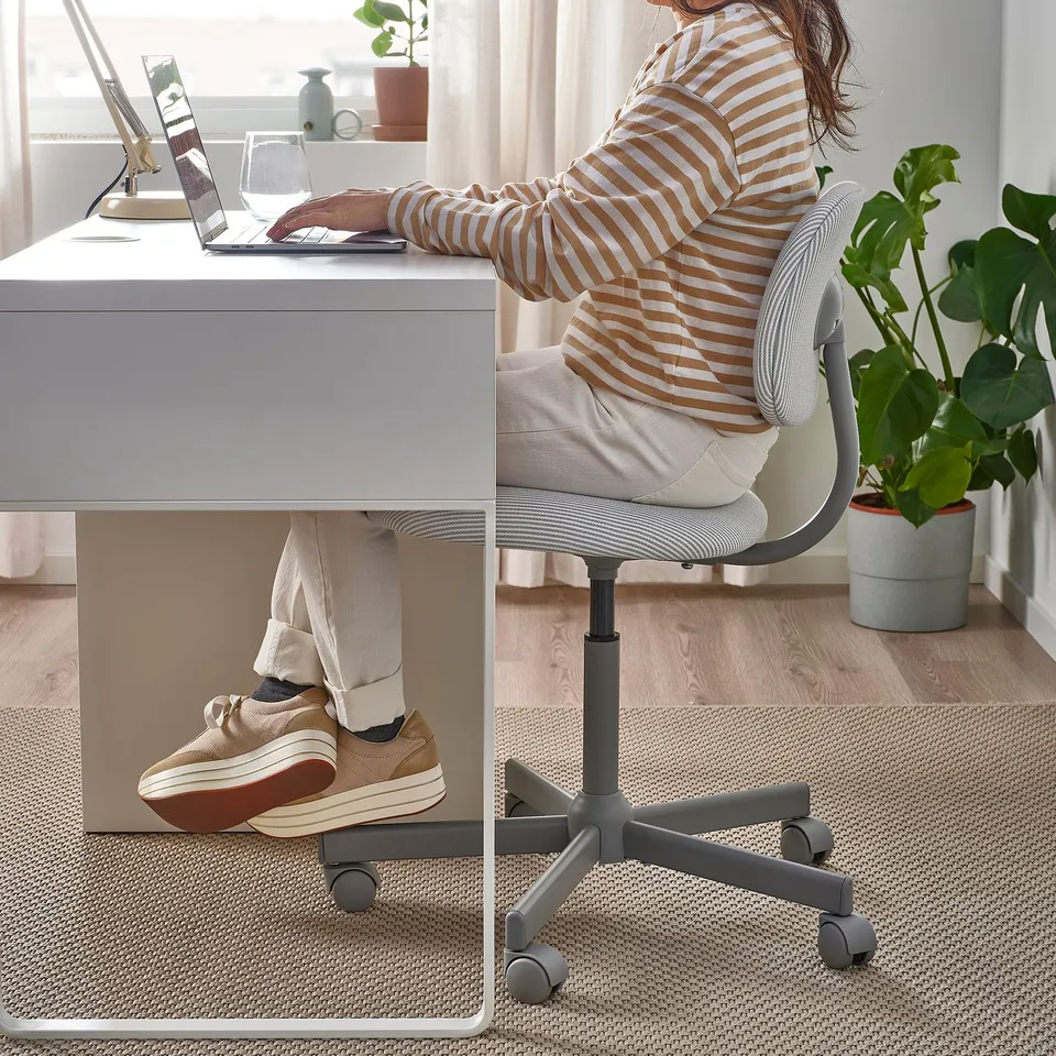 Person using laptop on BLECKBERGET chair, adjustable height, feet on floor.