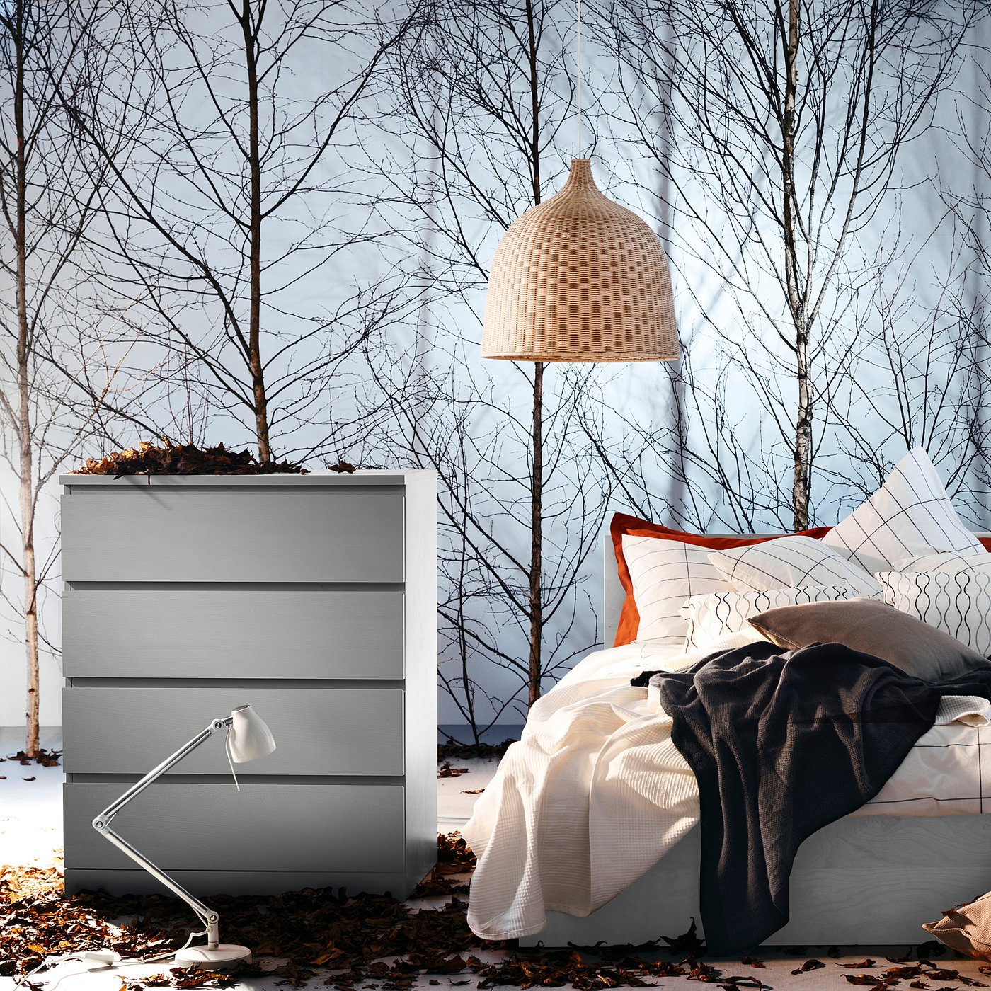 Cosy indoor scene with a light grey MALM chest and a white bed, adorned with white and grey pillows, under a large wicker pendant lamp.