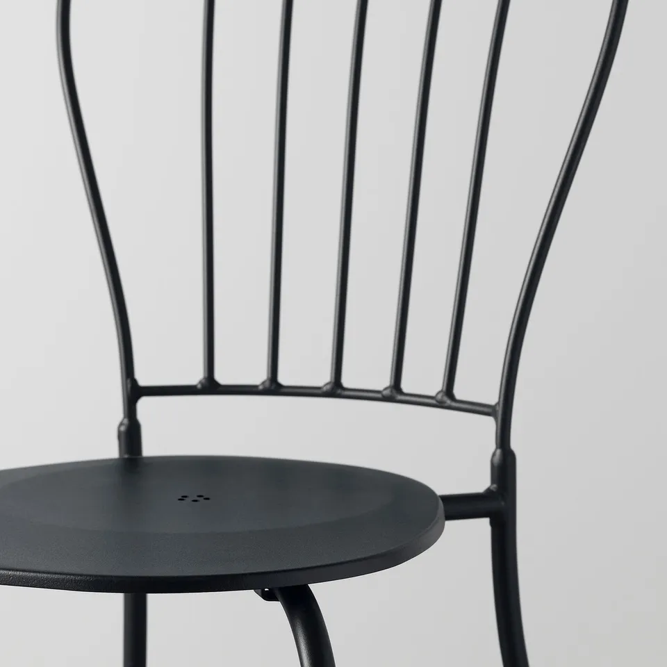 Black metal chair with round seat, designed for outdoors, featuring drain hole and stackable design.