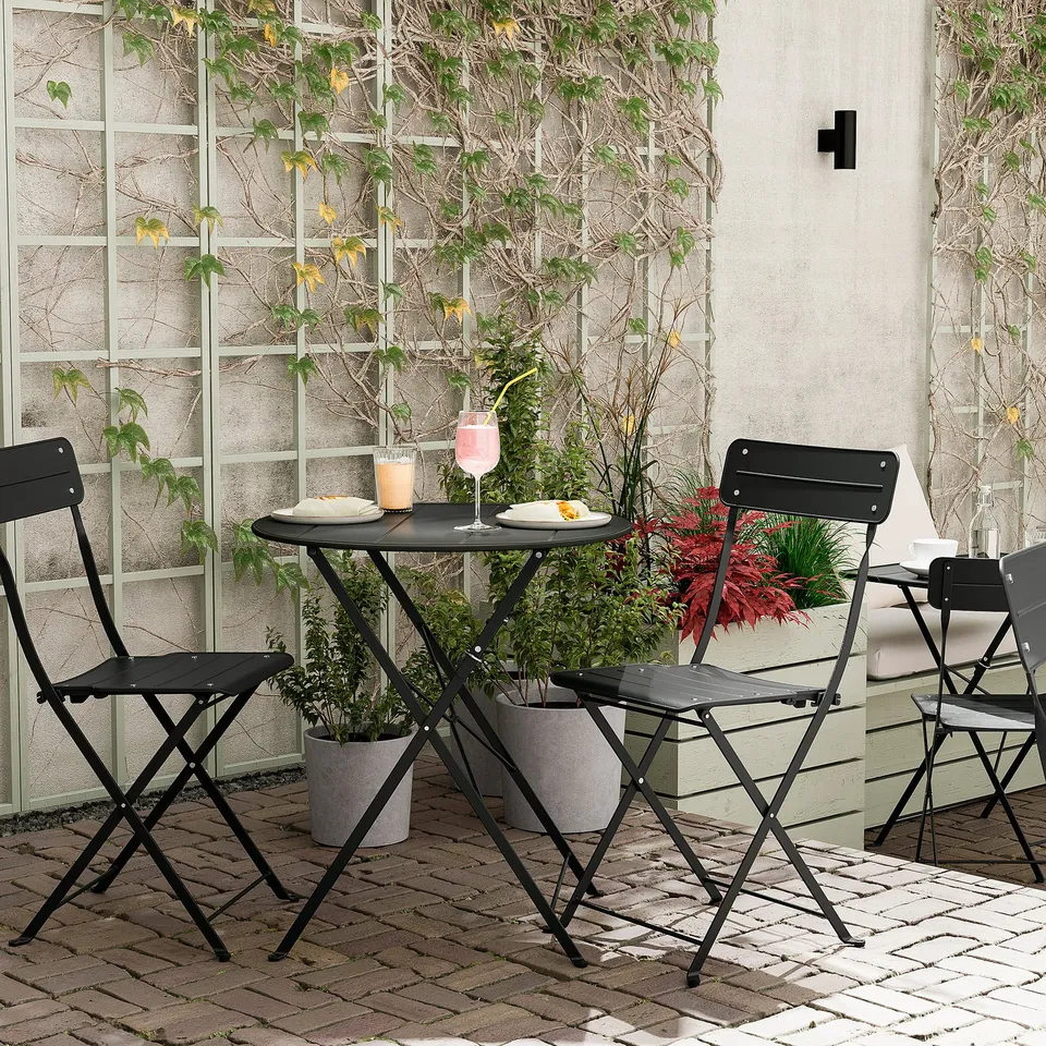 Three black SUNDSÖ folding chairs around a black table on a brick patio, set with plates and drinks.