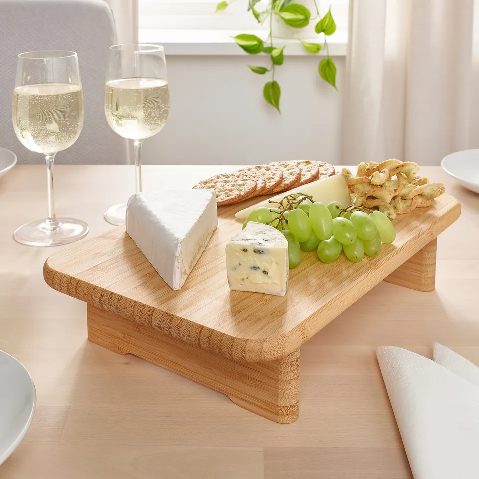 Wooden cheese board with crackers, grapes, and cheese blocks; two wine glasses nearby.