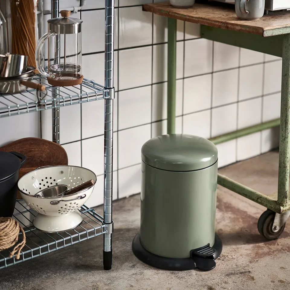 Small green step bin beside metal shelf with kitchen items.