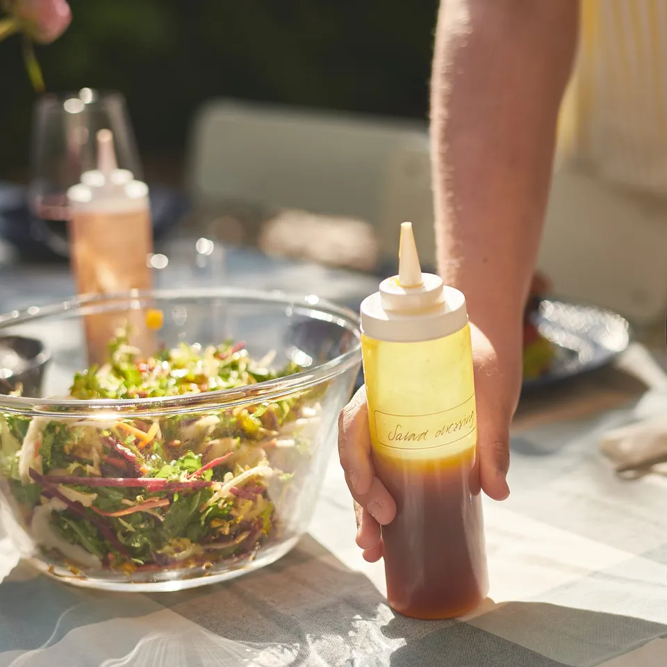 Person holding yellow squeeze bottle labelled jauna dressing over salad bowl.