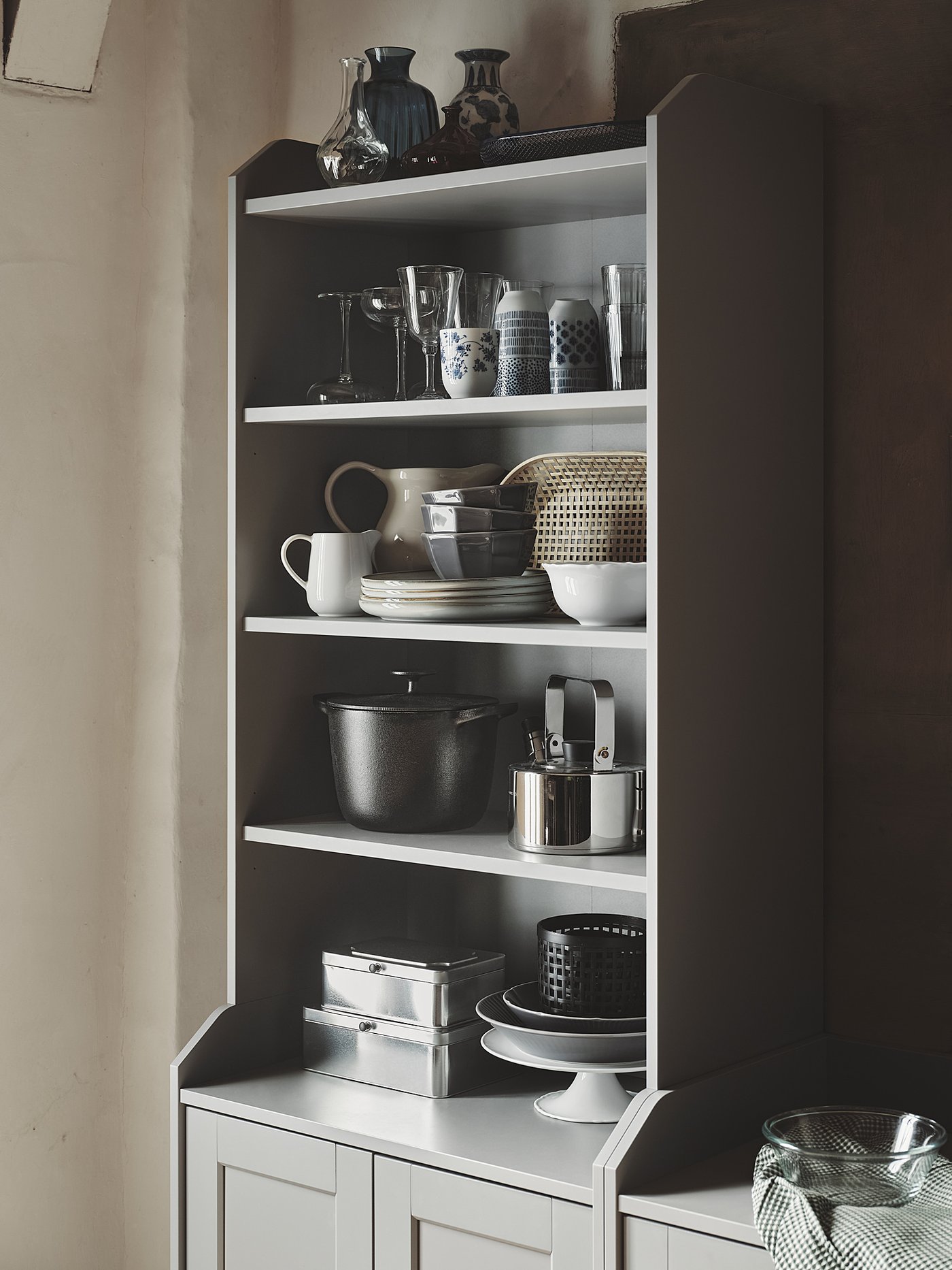 A white HAUGA cabinet with glassware, dishes, and cookware neatly arranged on open shelves. Black and silver accents.