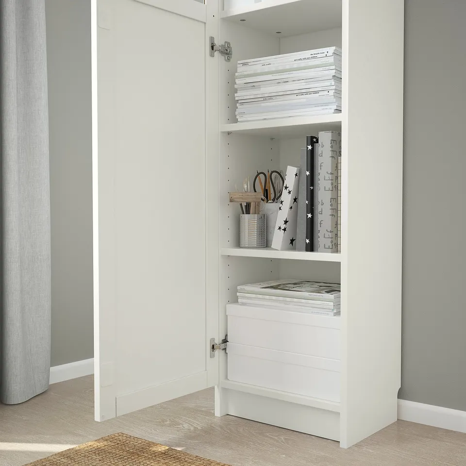 White BILLY bookcase with 3 shelves. Top and bottom hold books/papers. Middle shelf has stationery and star items. Anchored to grey wall.